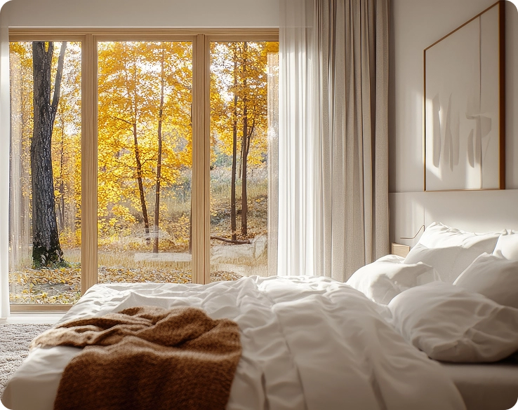 Een gezellige, lichte slaapkamer met een panoramisch raam en uitzicht op een herfstbos met gele bomen