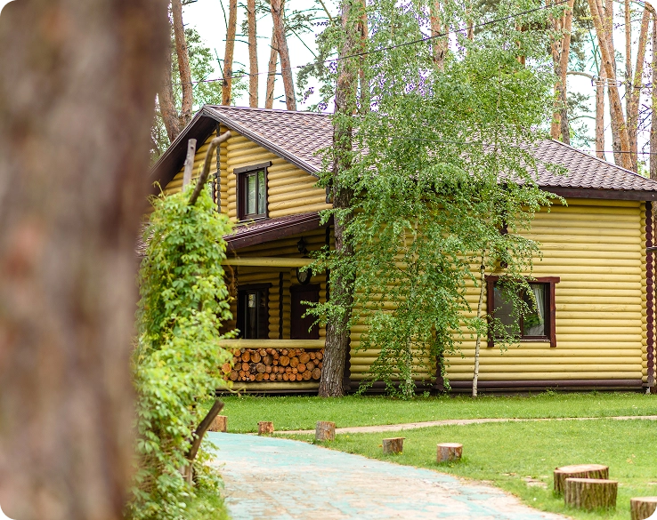 Een groot geel houten huisje staat in het bos, met keurige paadjes eromheen
