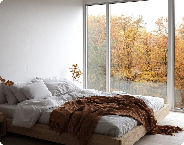 Een minimalistische slaapkamer met grijs beddengoed en een panoramisch raam met uitzicht op een herfstbos