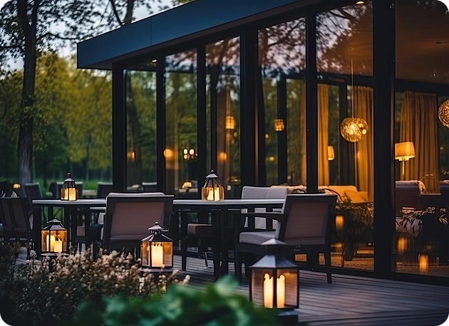 Het ruime terras van het restaurant met donker meubilair en ronde lampen, met uitzicht op het bos