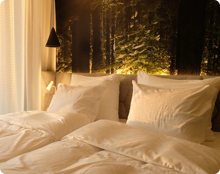 Een lichte kamer met een groot bed en zachte kussens aan het hoofdeinde, met fotobehang dat een bos weergeeft